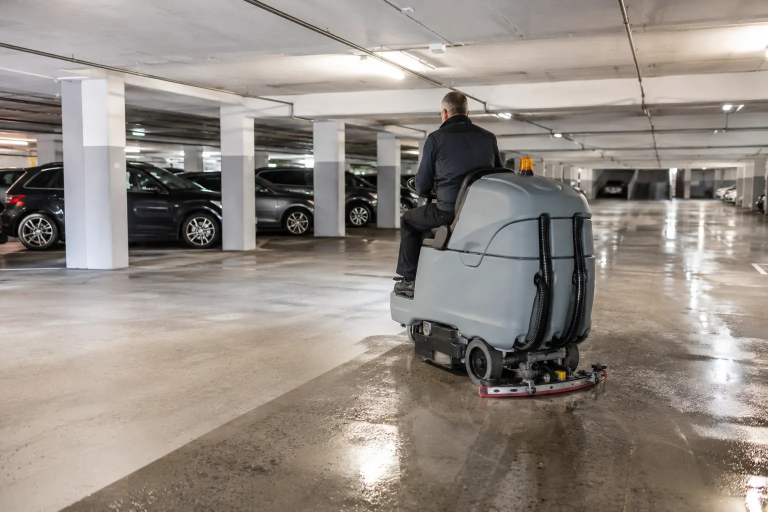Parking souterrain en cours de nettoyage, balayeuse aspirante sur les circulations, traitement d’une tache d’huile sur une place